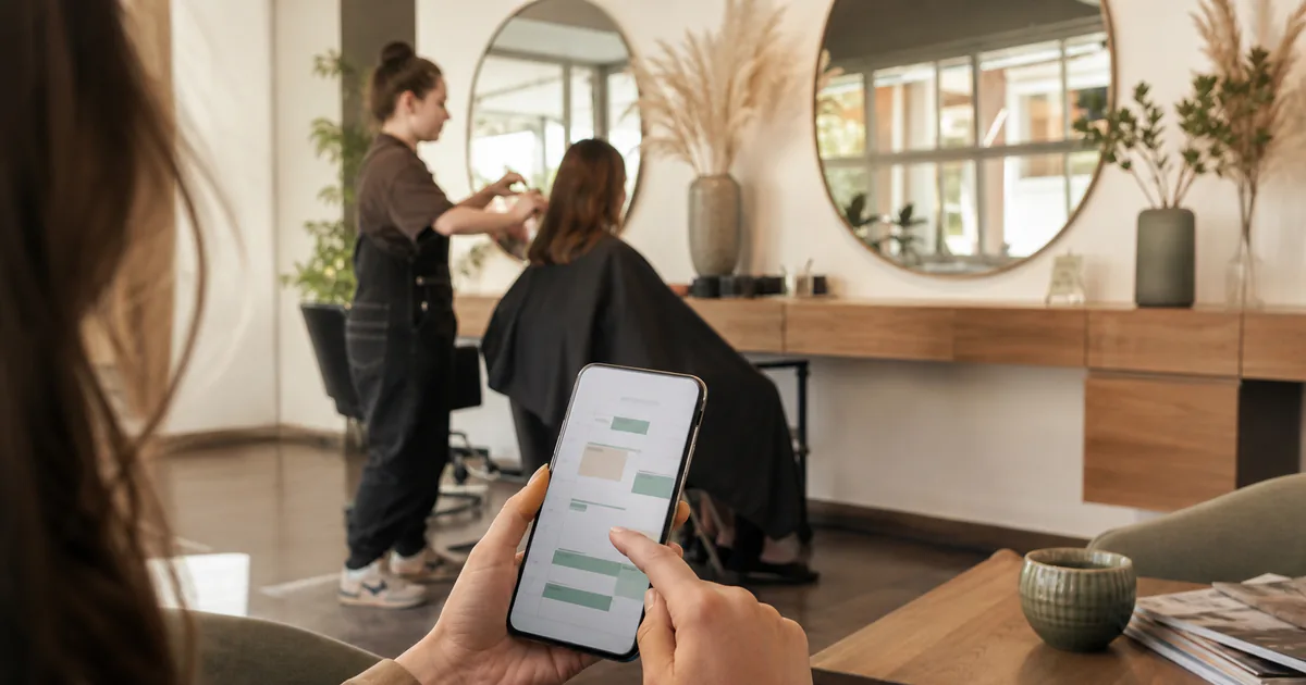 Kundin bucht einen Friseurtermin mobil, während im Hintergrund eine Behandlung stattfindet